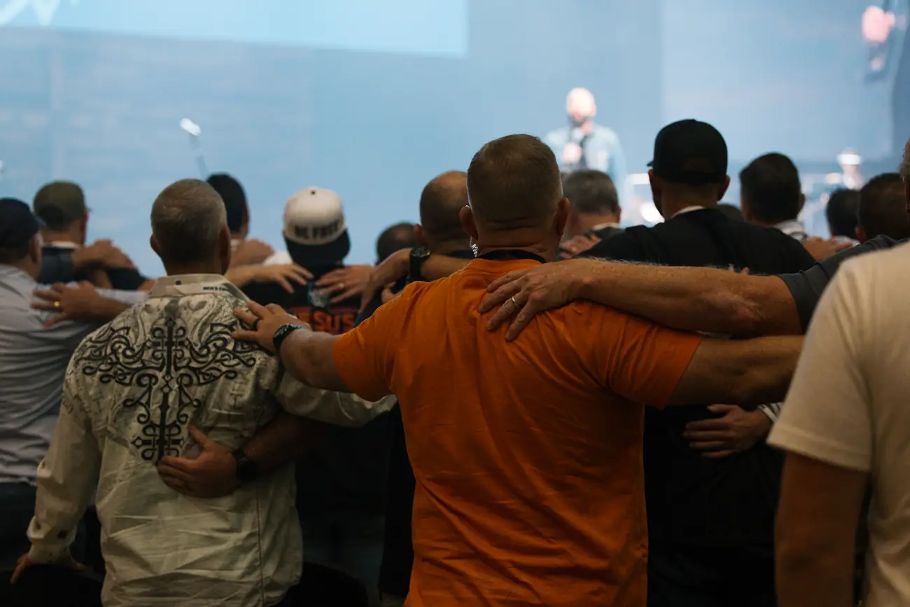 Men standing arm in arm, praying together at Men's Conference